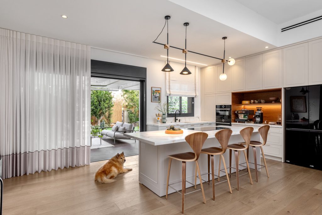 White kitchen with a marble island, wooden bar stools and black pendant lights
