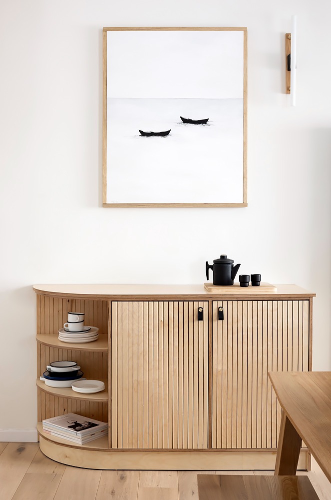 Fluted wooden sideboard with rounded shelves below an artwork