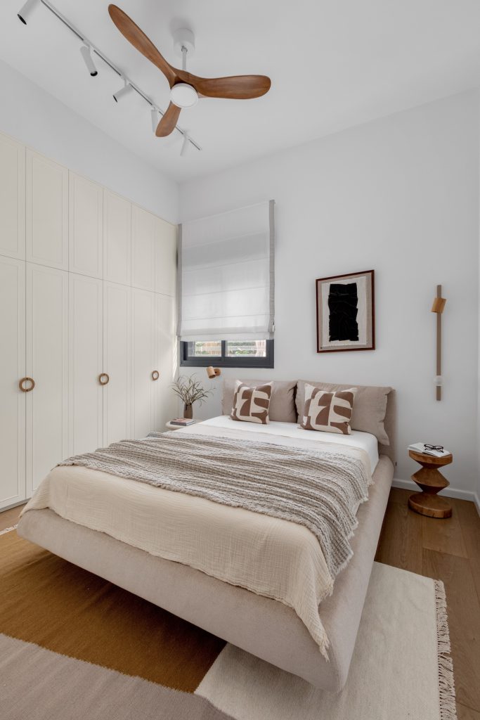 Beige bedroom with a wooden ceiling fan and white wardrobes