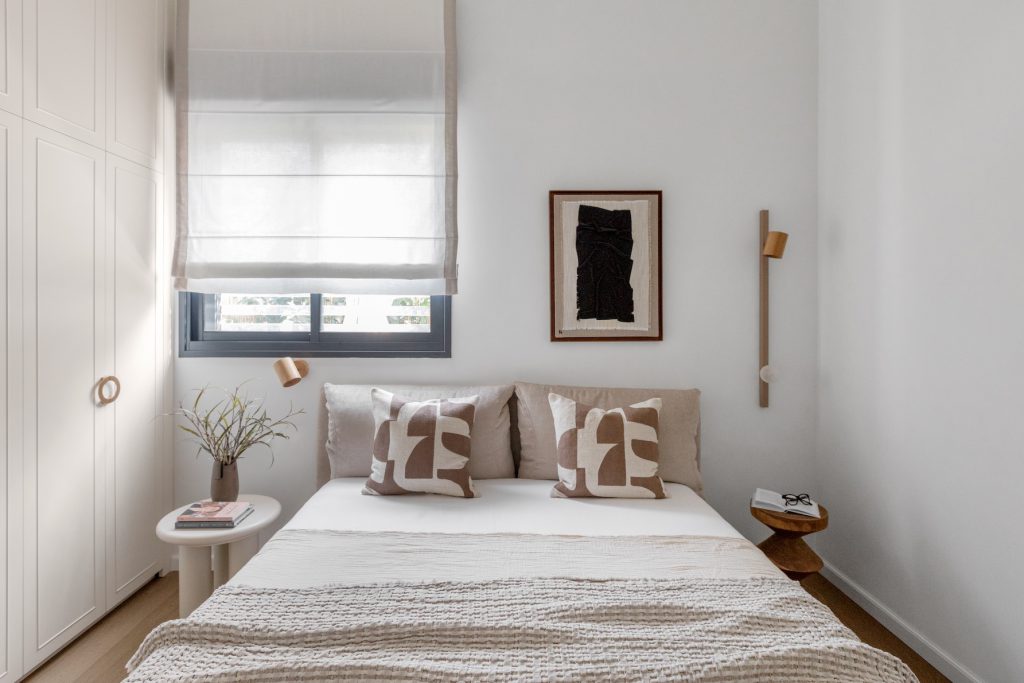 Double bed with patterned cushions, a Roman blind and a black artwork