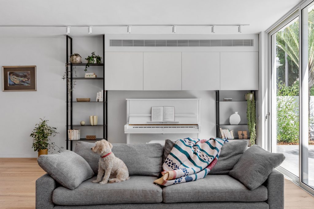 Grey sofa facing a white piano between black shelves