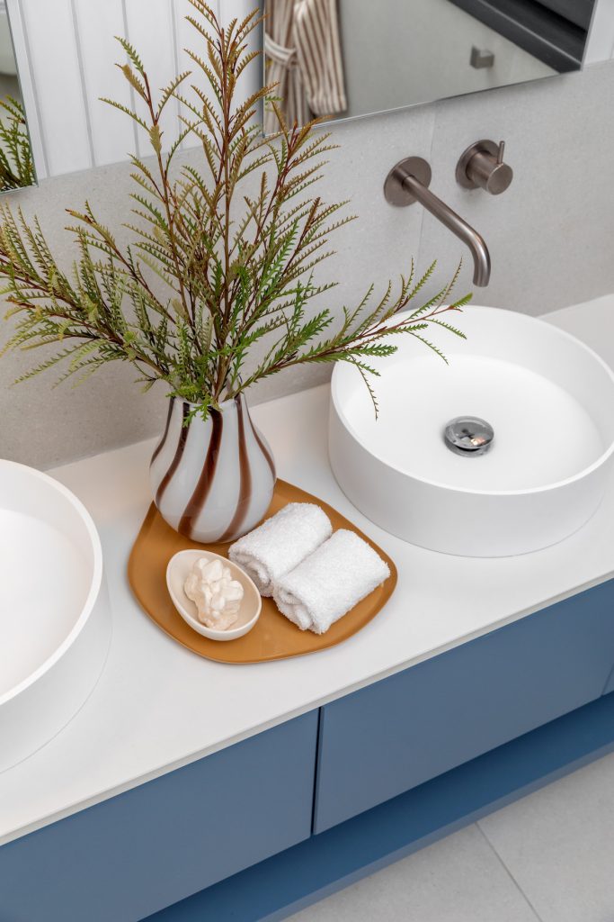 Detail: white bowl basin on a blue vanity with a copper-tone tap