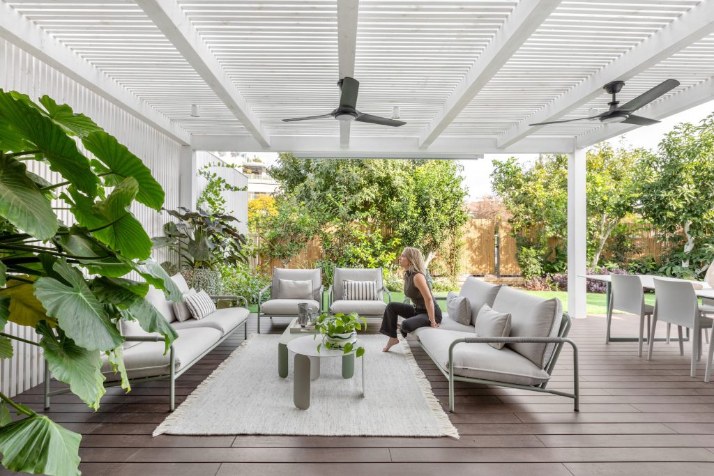 White pergola over a timber deck with outdoor sofas and a ceiling fan
