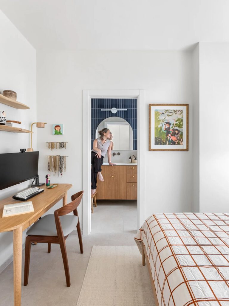 Bedroom with a wooden desk and a view into a blue-tiled bathroom