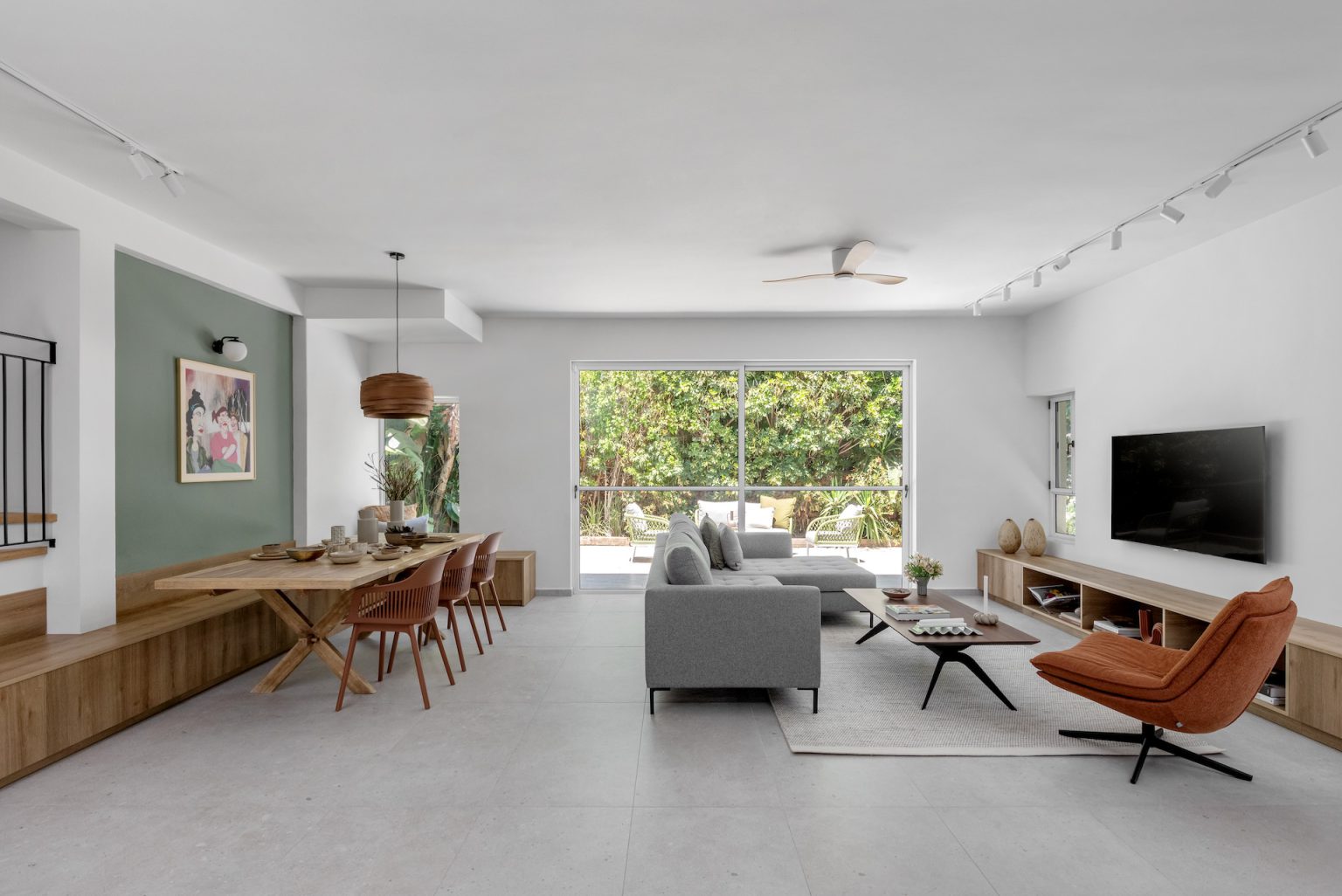 Open space with a grey sofa, a rust armchair and a dining area facing the garden