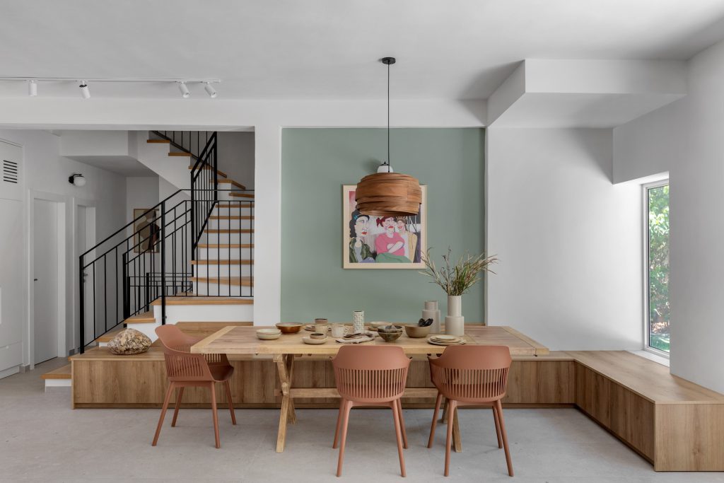 Dining area with a U-shaped wooden bench and a sage-green wall