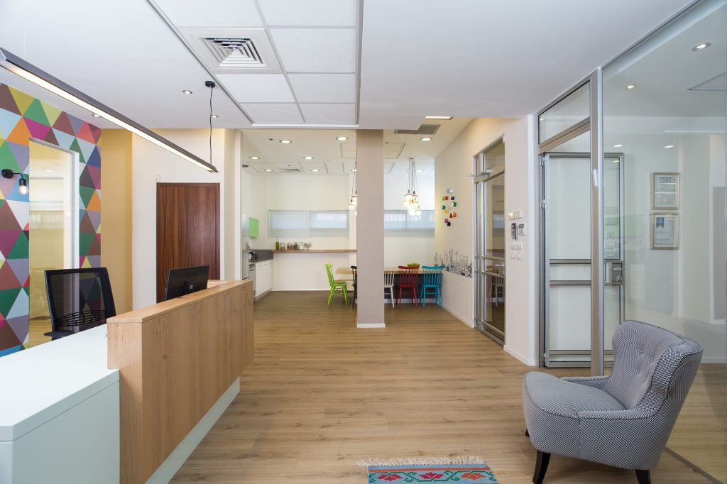 Lobby with a wooden desk, a grey armchair and a colourful triangle wall, Gita Technologies offices in Tel Aviv – Chen Shadmi, Shadmi Design