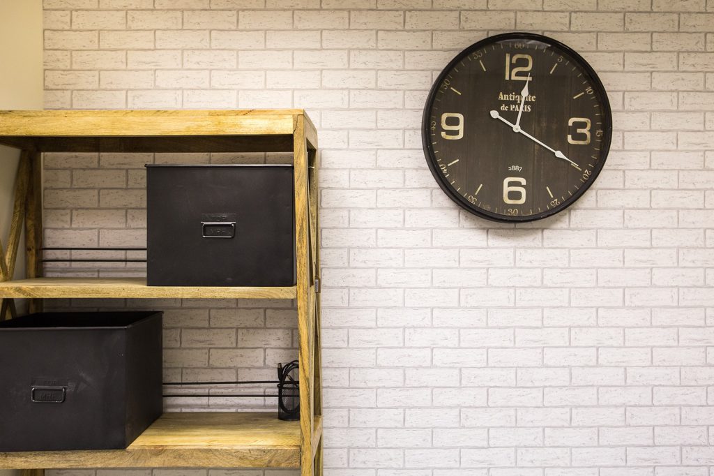 Detail: wall clock and wooden shelving on a white brick wall