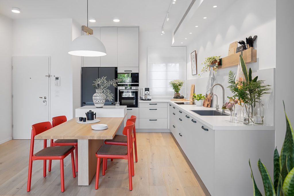 L-shaped white kitchen with a wooden table and red chairs