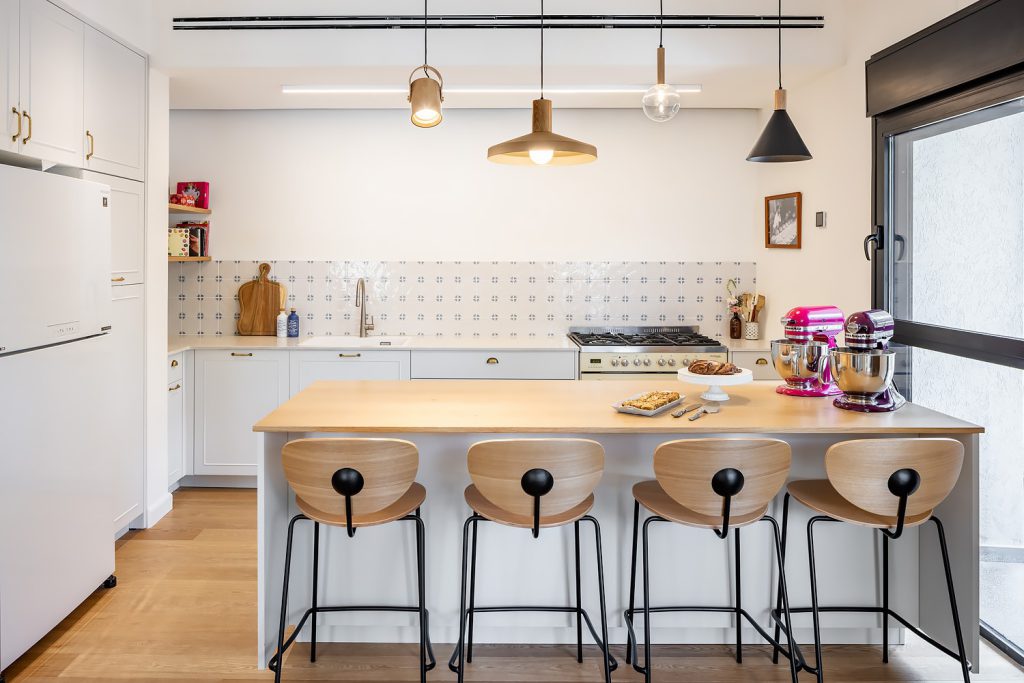 White kitchen with a wooden counter, sculpted bar stools and pendant lights
