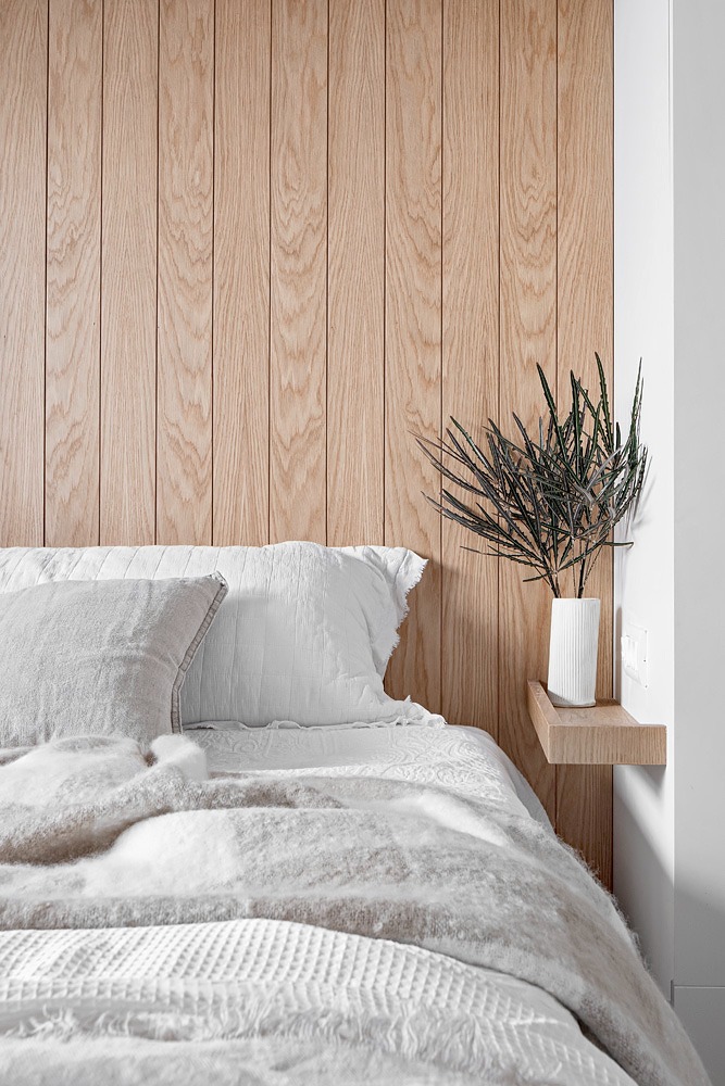 Bed against a wood-panelled wall with a floating bedside shelf