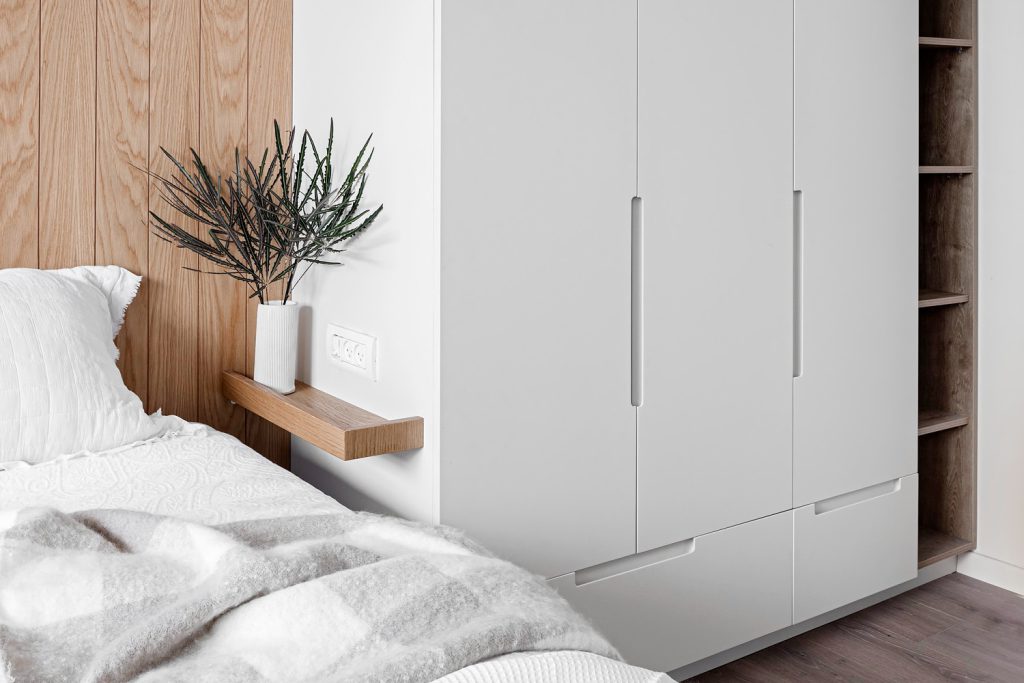 White wardrobe beside the wooden wall and bedside shelf