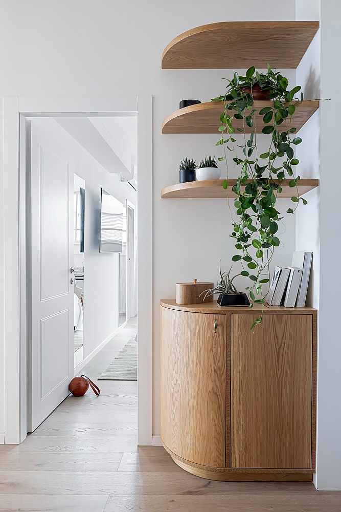 Rounded wooden cabinet and floating shelves with plants in the hallway