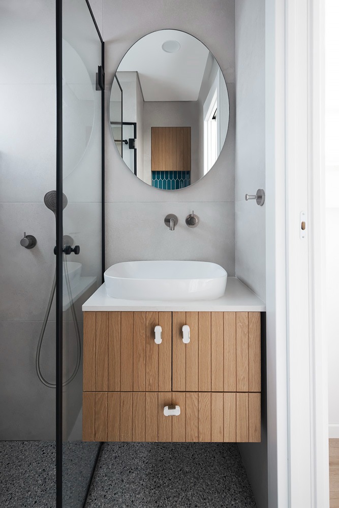 Wooden vanity and round mirror beside a glass shower