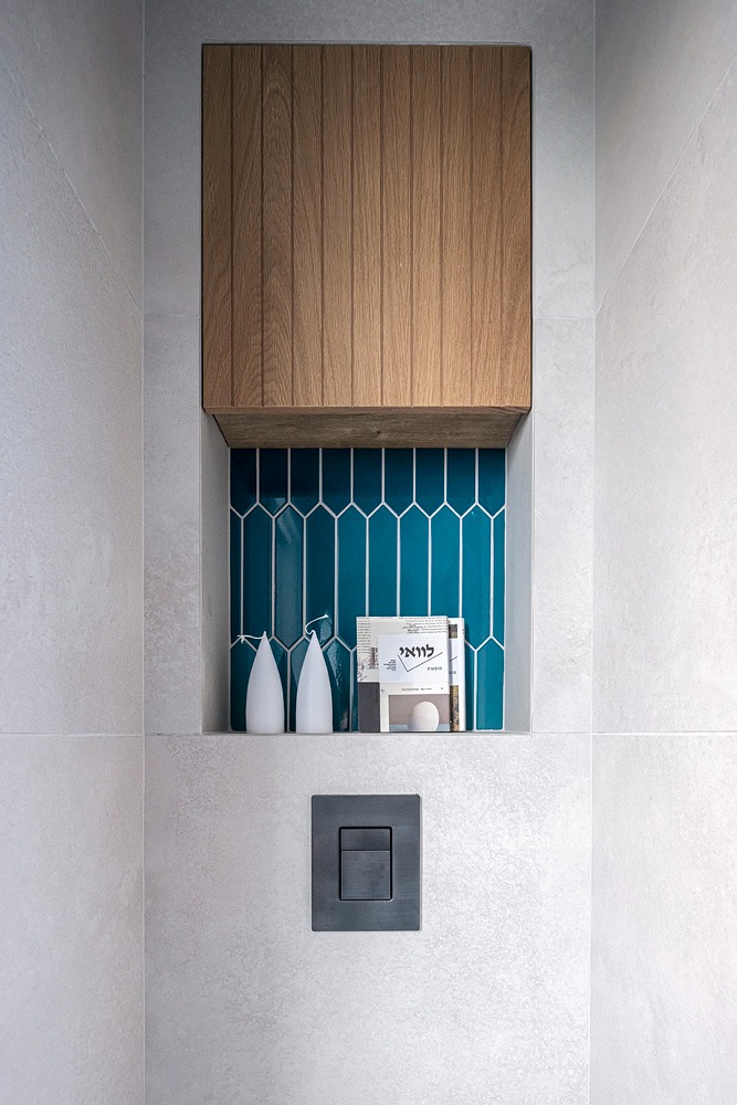 Wall-hung wooden cabinet above a teal tile niche in the toilet