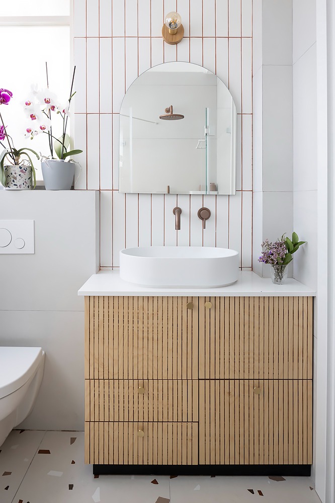 Bathroom with a fluted wooden vanity, white tiles and terrazzo