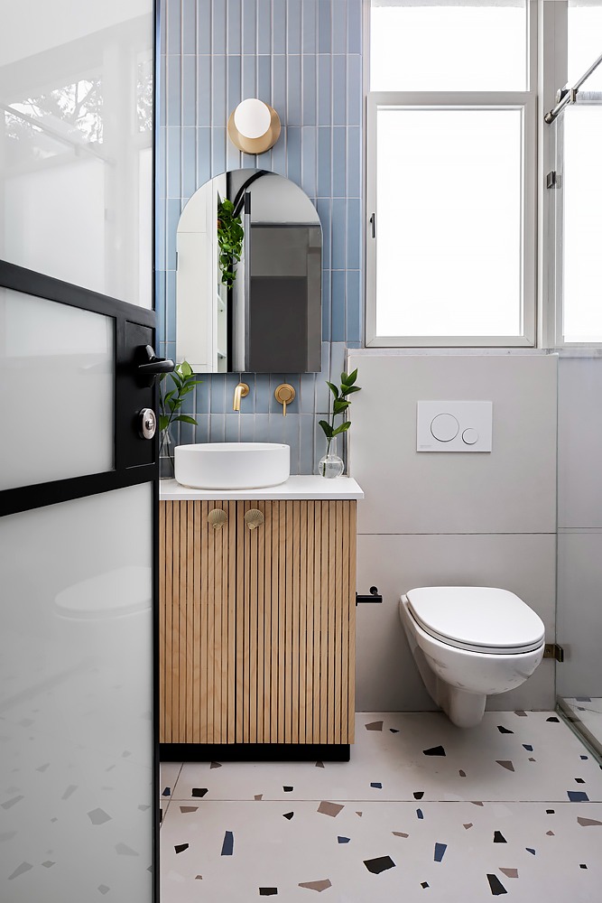 Toilet with long pale blue tiles and a fluted wooden vanity