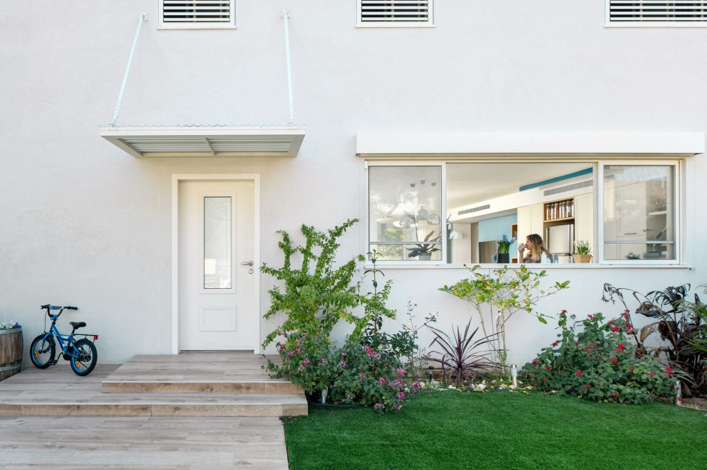 House front with a white door, a timber deck and a garden