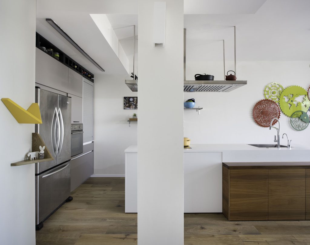 White kitchen with a suspended steel hood and a stainless fridge