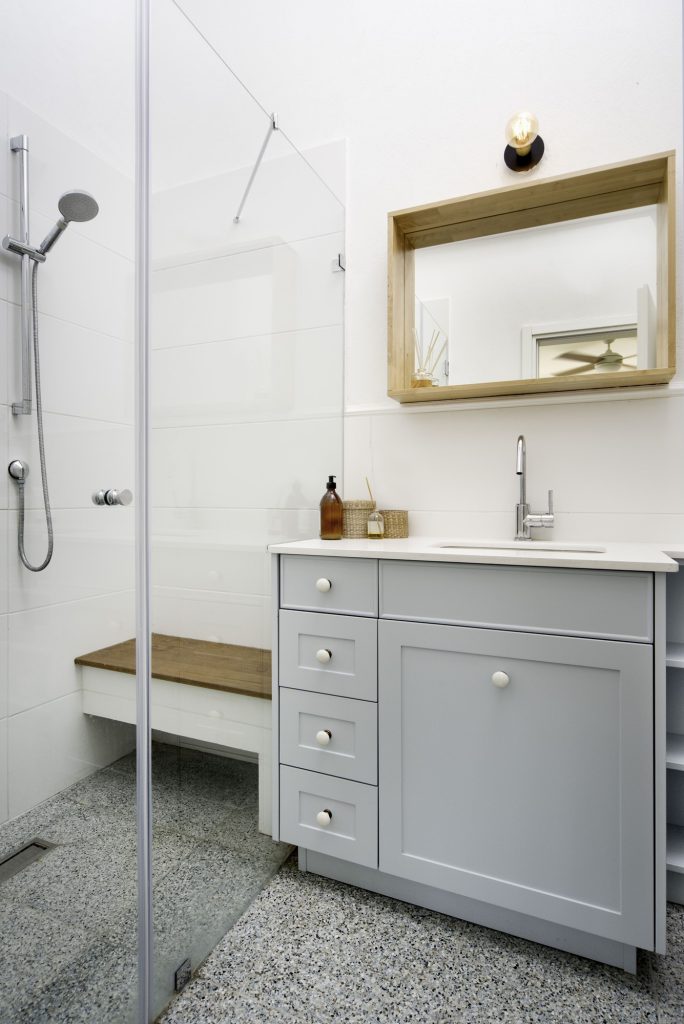 Bathroom with a grey vanity and a wooden shelf above