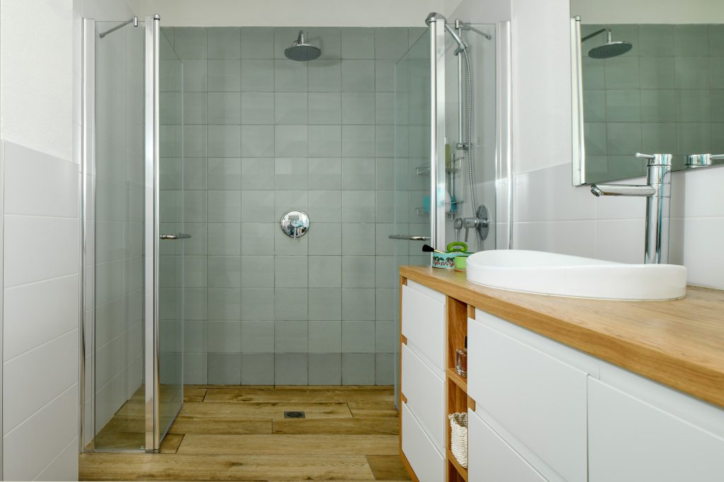 Shower with grey-green tiles and a wooden counter