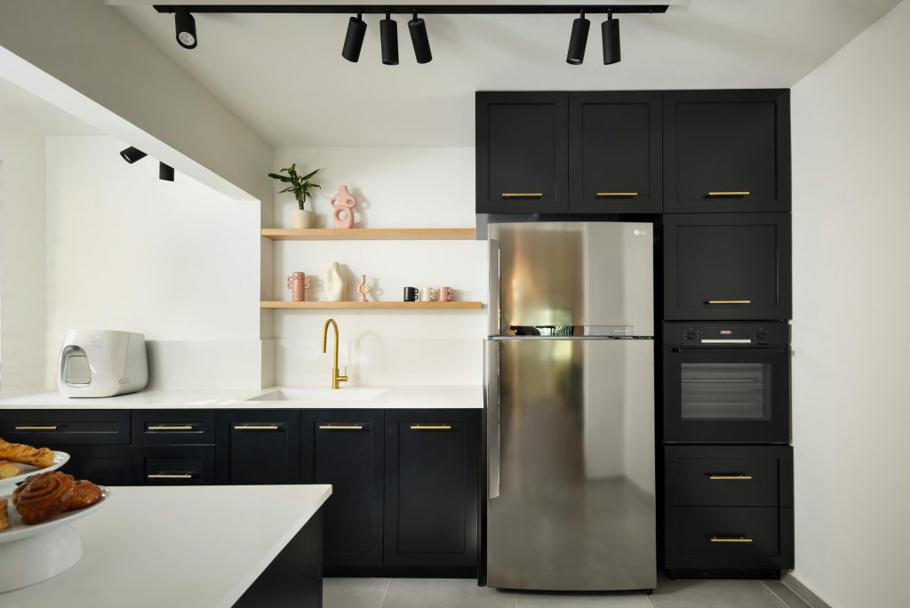 Black kitchen with a stainless fridge and track lighting