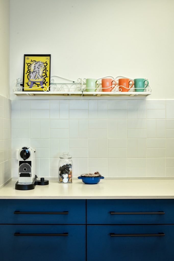 Kitchenette with blue cabinets and a shelf of colourful mugs