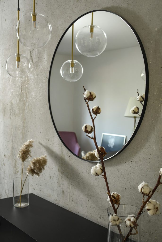 Detail: oval mirror and glass pendants on a concrete wall